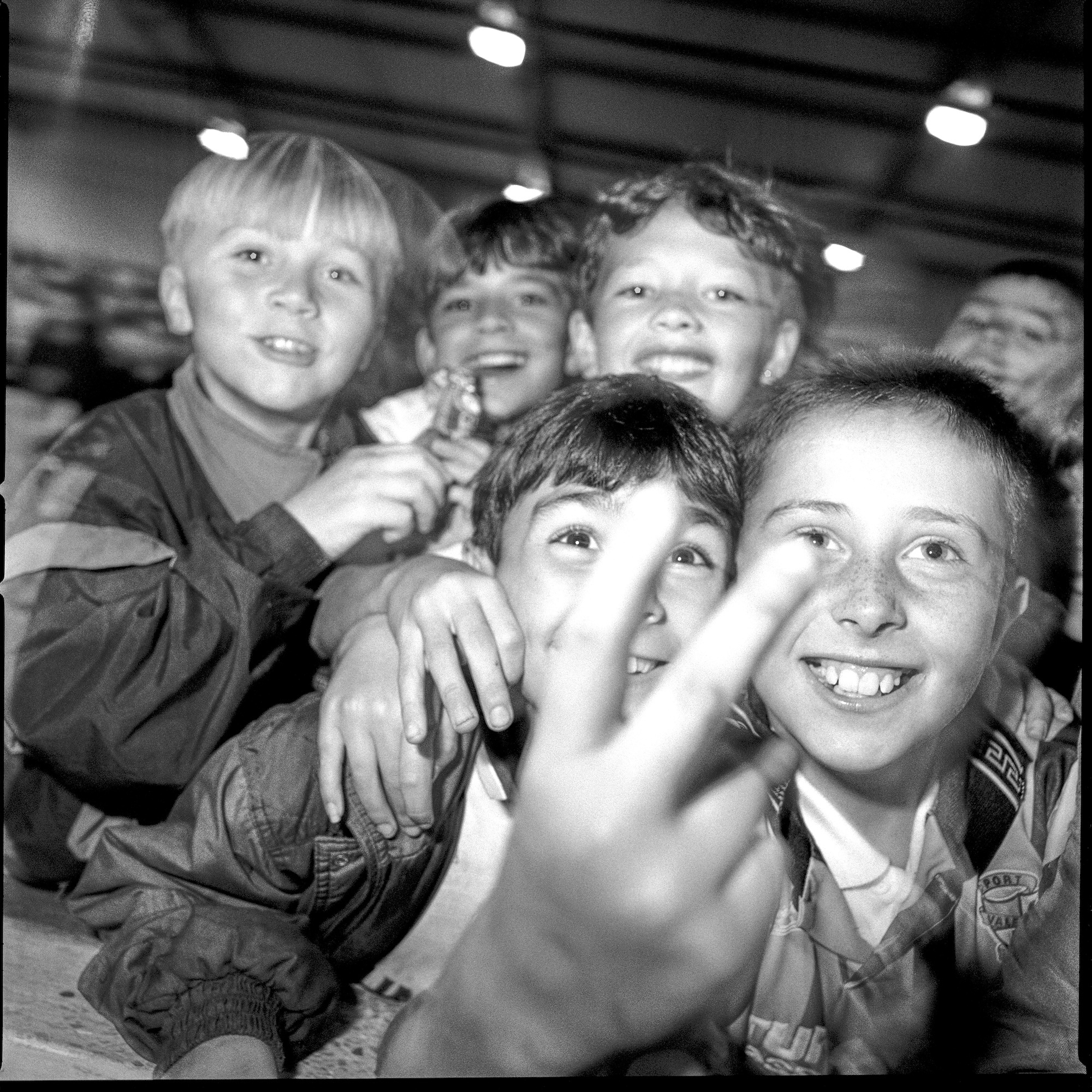 Black and white photo of several young people smiling at the camera, one holding two fingers up.