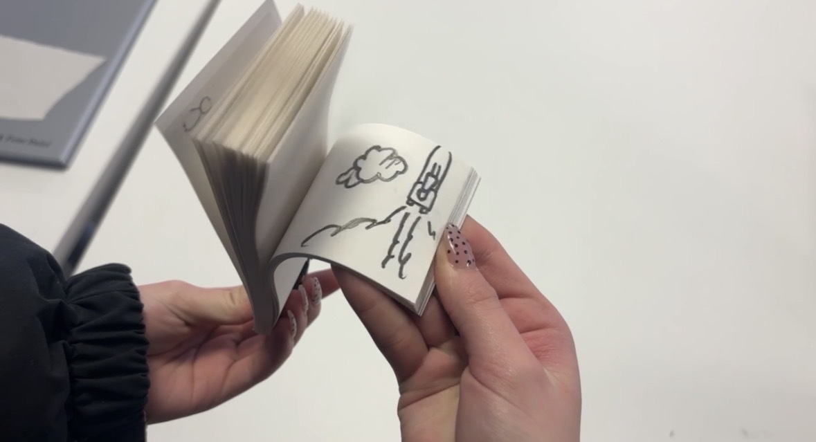 Hands holding open a small flipbook showing simple line drawings that create animation when pages are flipped quickly.