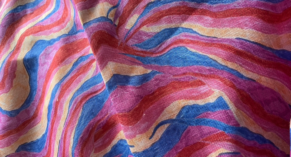 Flowing fabric with wavy horizontal stripes in pink, blue, purple, and cream colours creating curved folds and shadows.