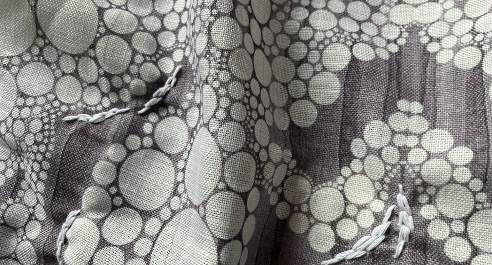 Crumpled fabric with grey, white and brown circular dot pattern in varying sizes across textured surface.