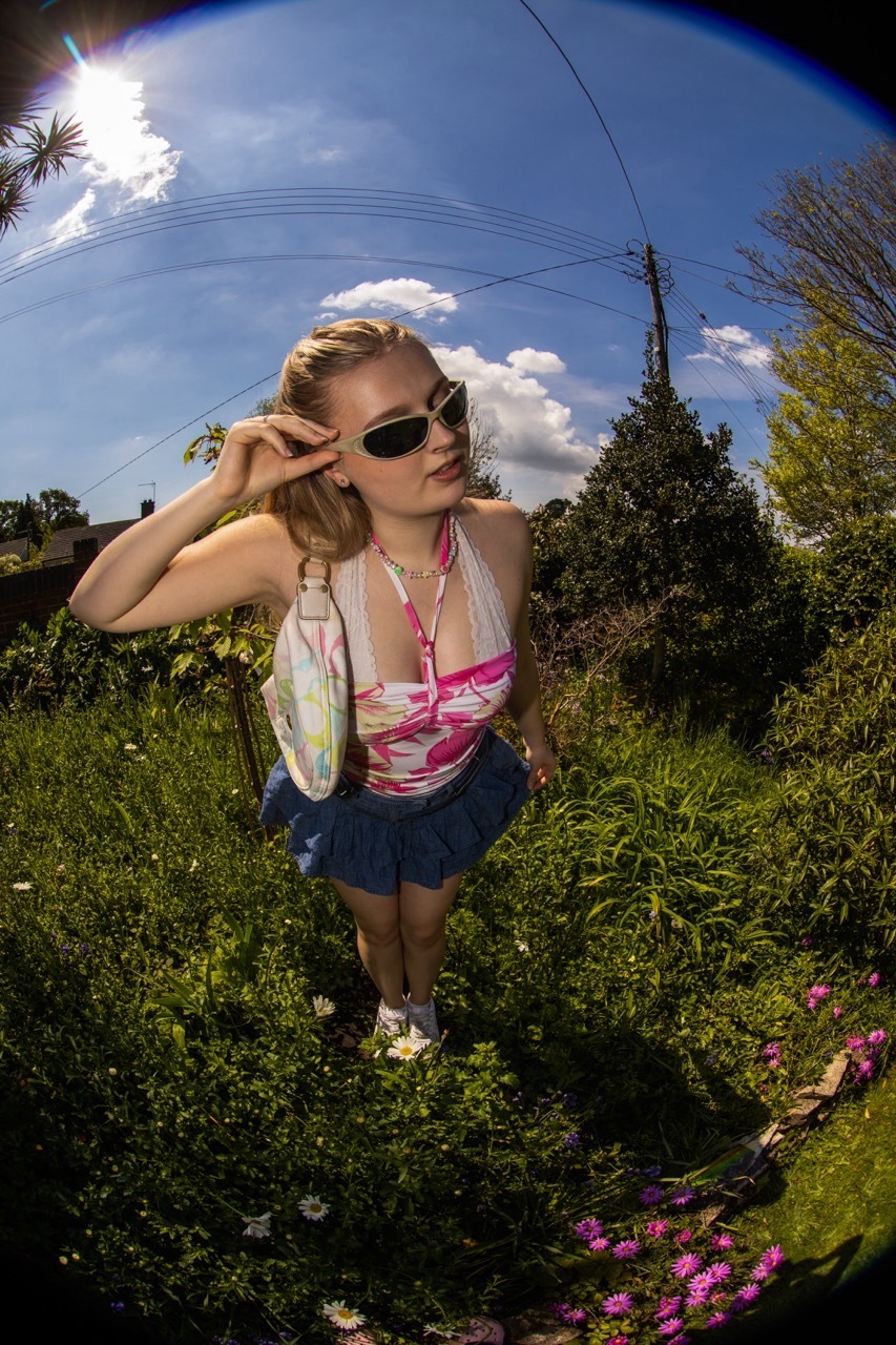Model in flashy clothing stood outside in the sun, fisheye lens shot.