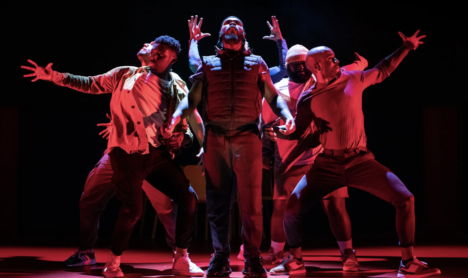 A group of actors under red lighting mid-performance of R Calais Cameron's "For Black Boys Who Have Considered Suicide When The Hue Gets Too Heavy"