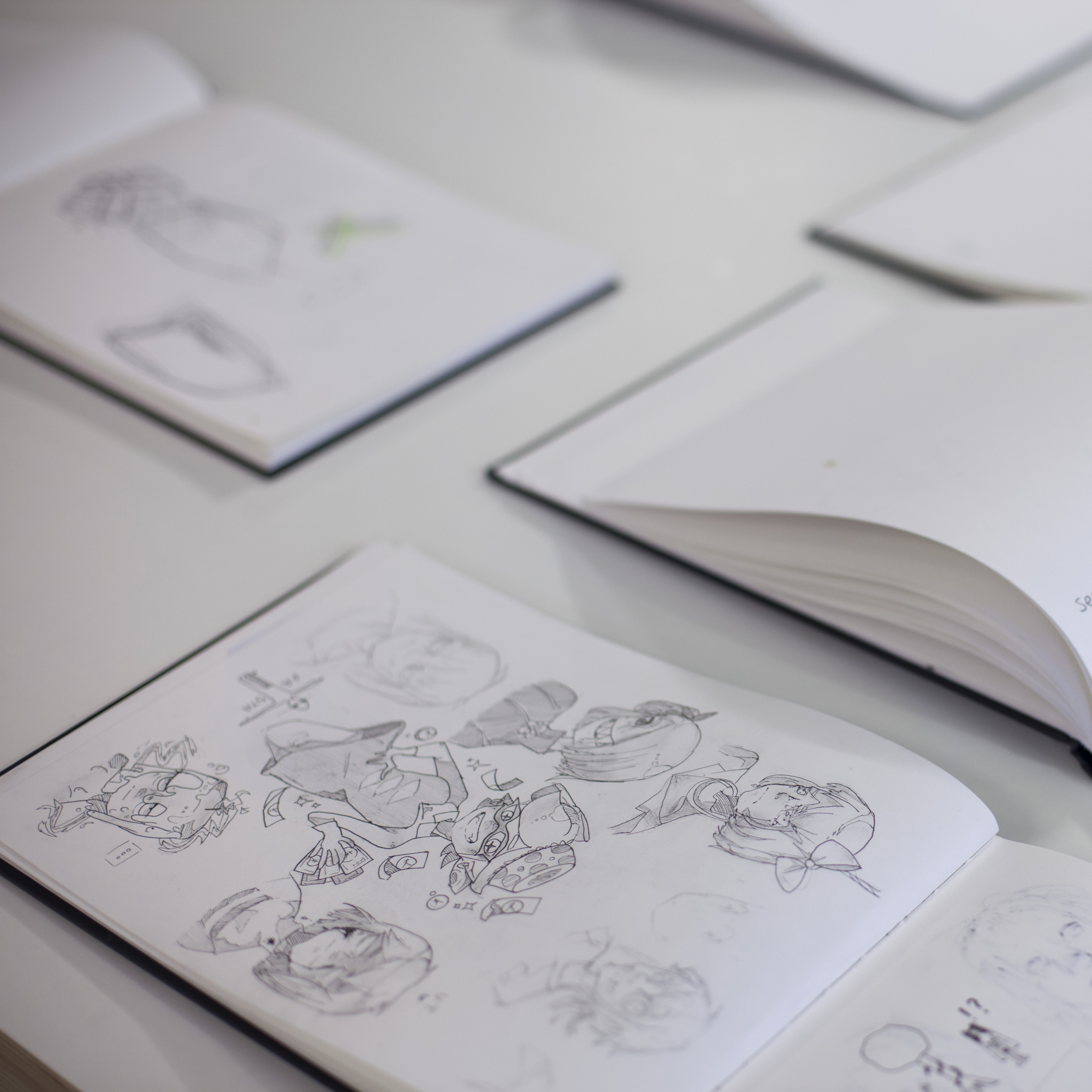 Several sketchbooks lying open on a table, with pencil drawings showing on the pages.