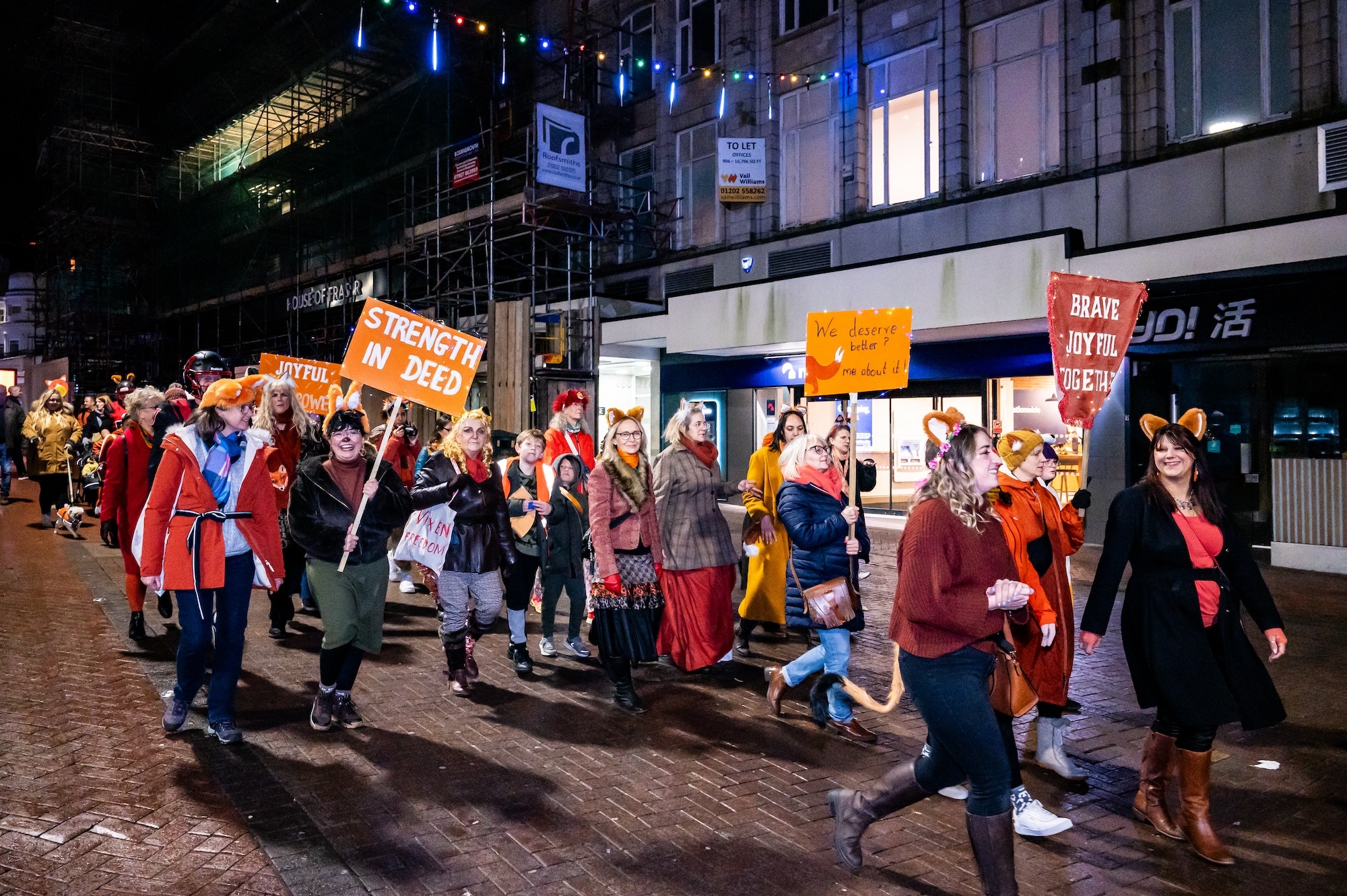 A large group of people walking down Bournemouth high street wearing fox ears and other fox-inspired clothing. Some of them are carrying placards.