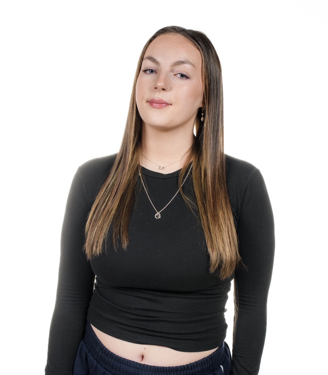 Woman with long brown hair wearing black long-sleeved top and layered necklaces against white background.