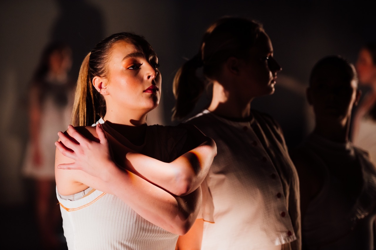 Two people dancing closely in dim lighting, woman in white top with blonde hair pulled back, man in dark clothing facing away.