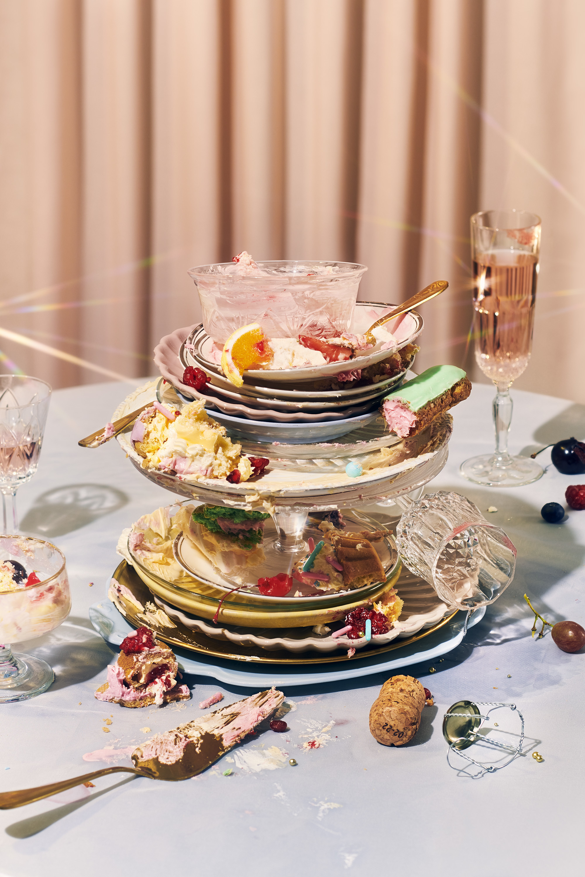A stack of different-sized plates with half-eaten food, surrounded by dirty forks, bowls, champagne corks and glasses of champagne.