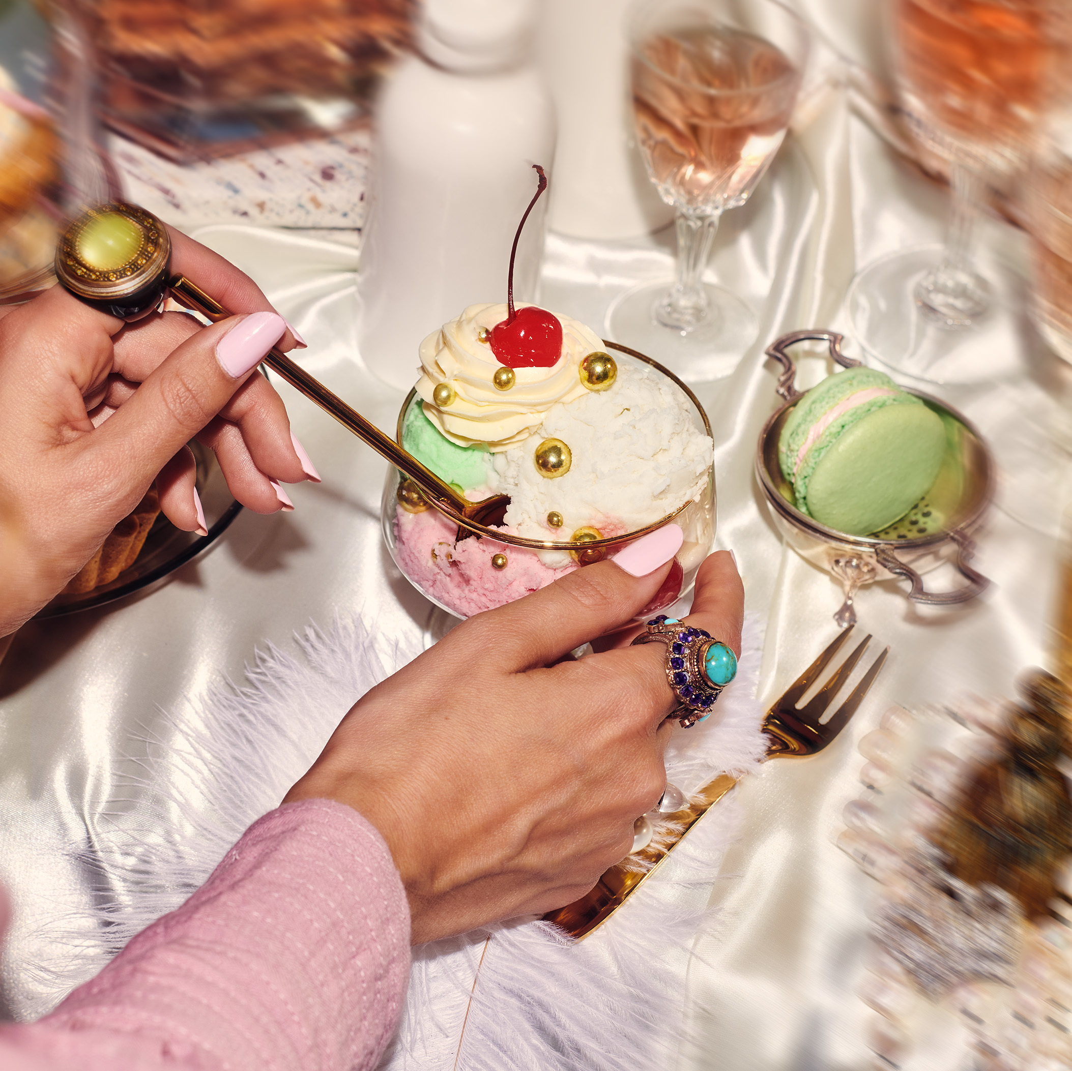 Close-up of a person's hands as they dip a long spoon into a dessert topped with whipped cream and a cherry.