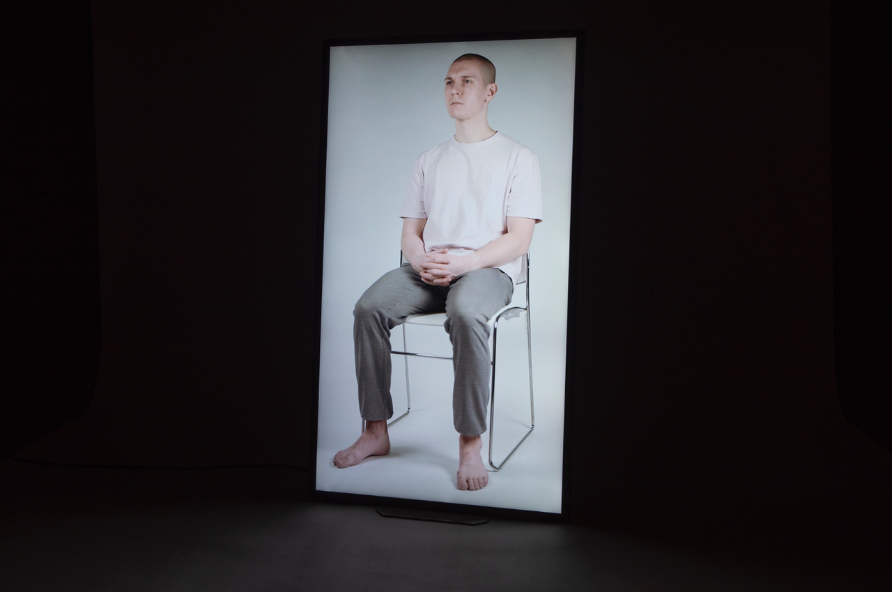 A person sitting on a chair barefoot and with their fingers crossed, having their photo taken.