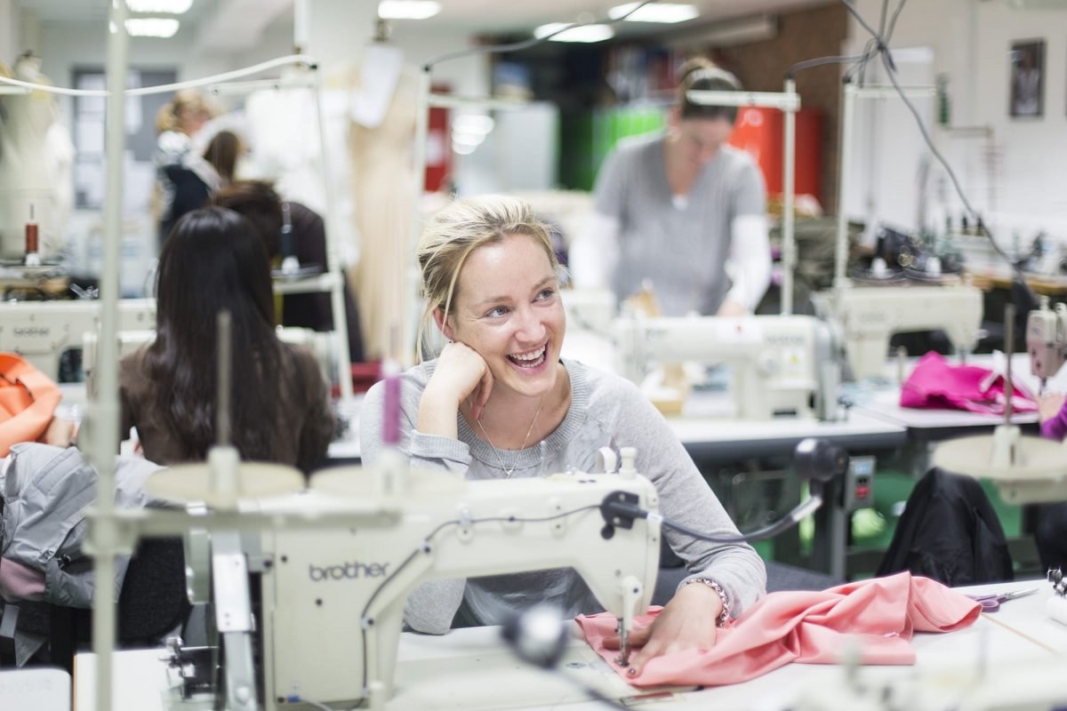 A person sits smiling at a desk with a sewing machine on it.