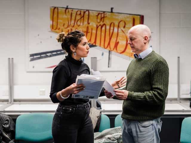 Two actors reading from scripts in the middle of a rehearsal.
