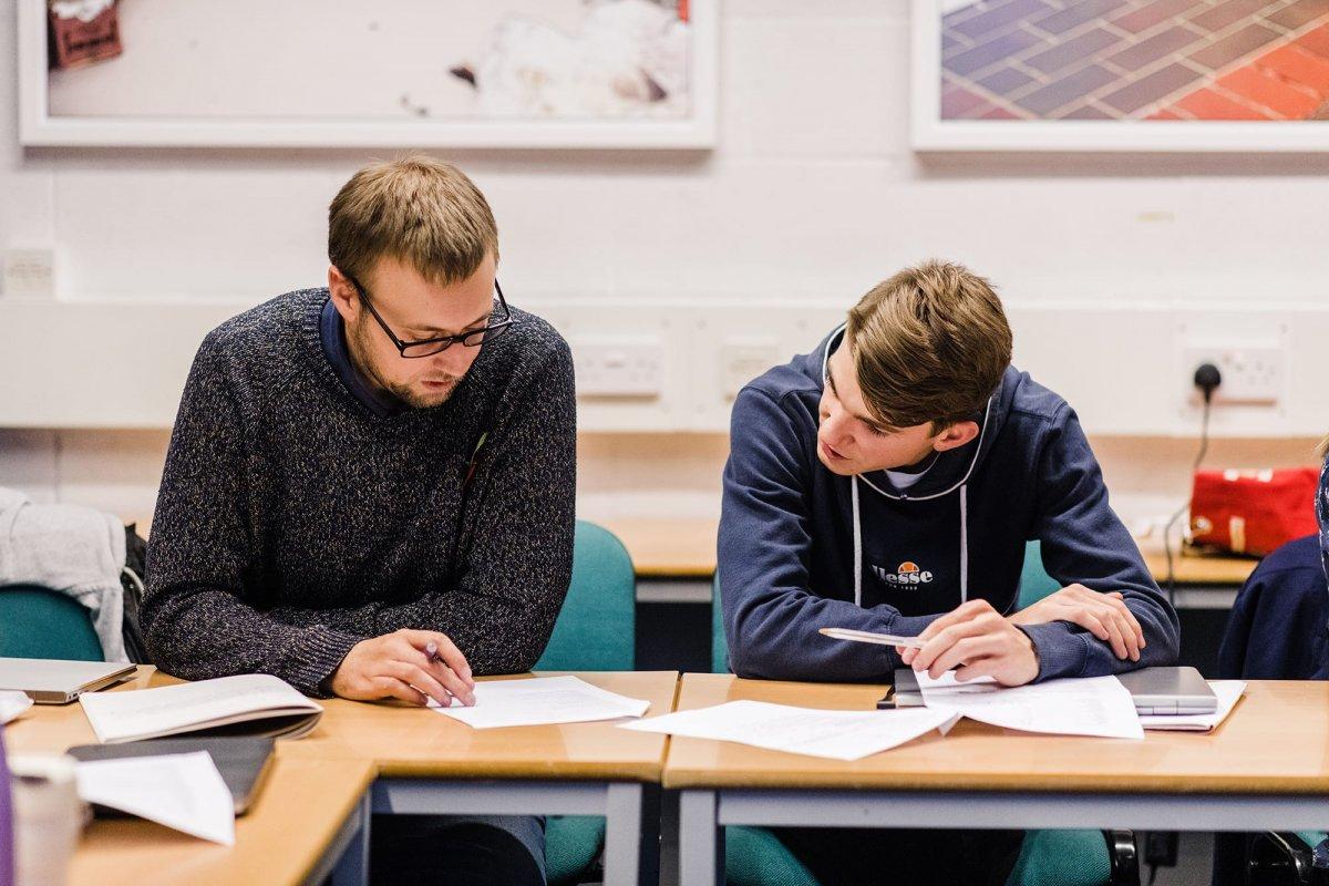 Two students having a discussion over several pieces of paper.