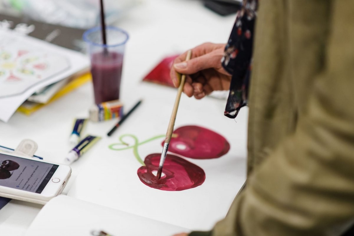 A student stands painting two cherries in a sketch book.