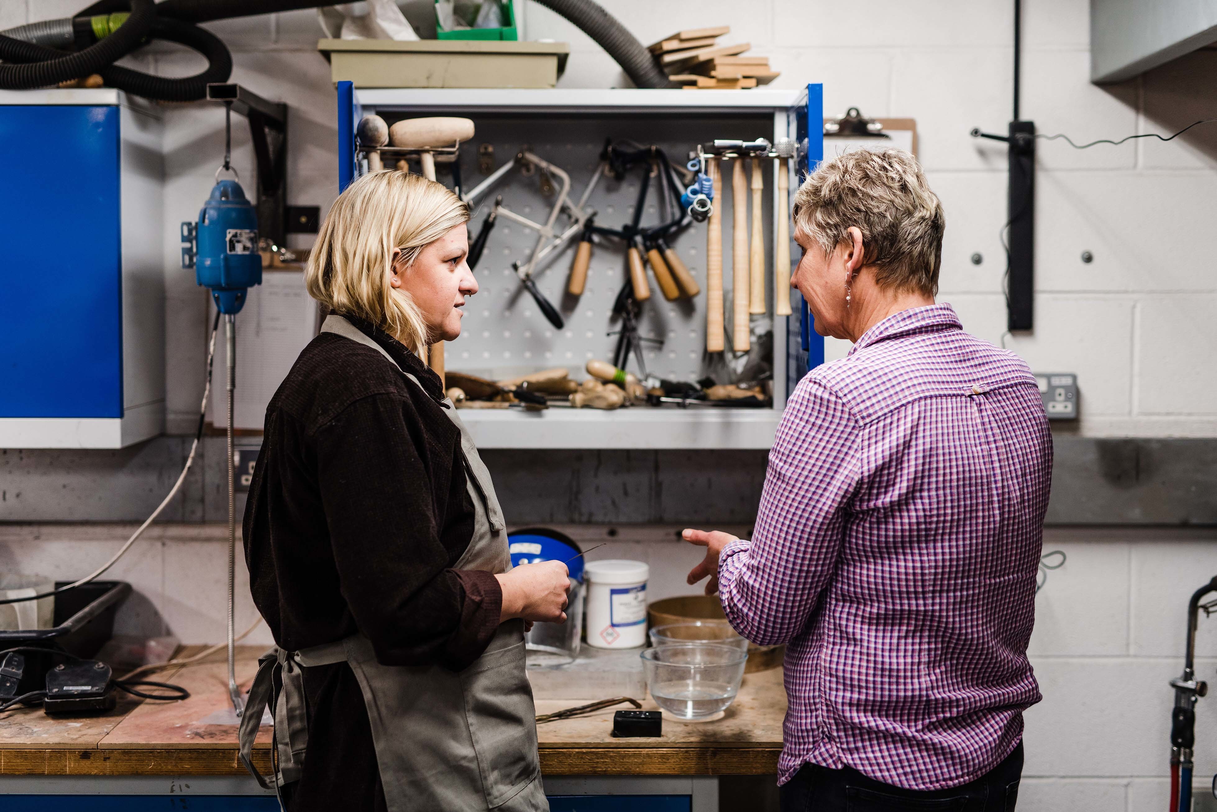 Two students talking by a table in a workshop.