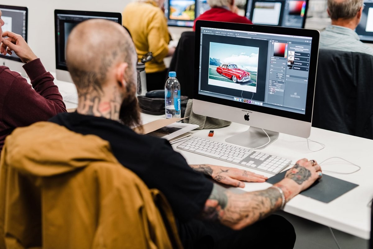 Image of a man sitting at a desk using Photoshop on an Apple Mac.