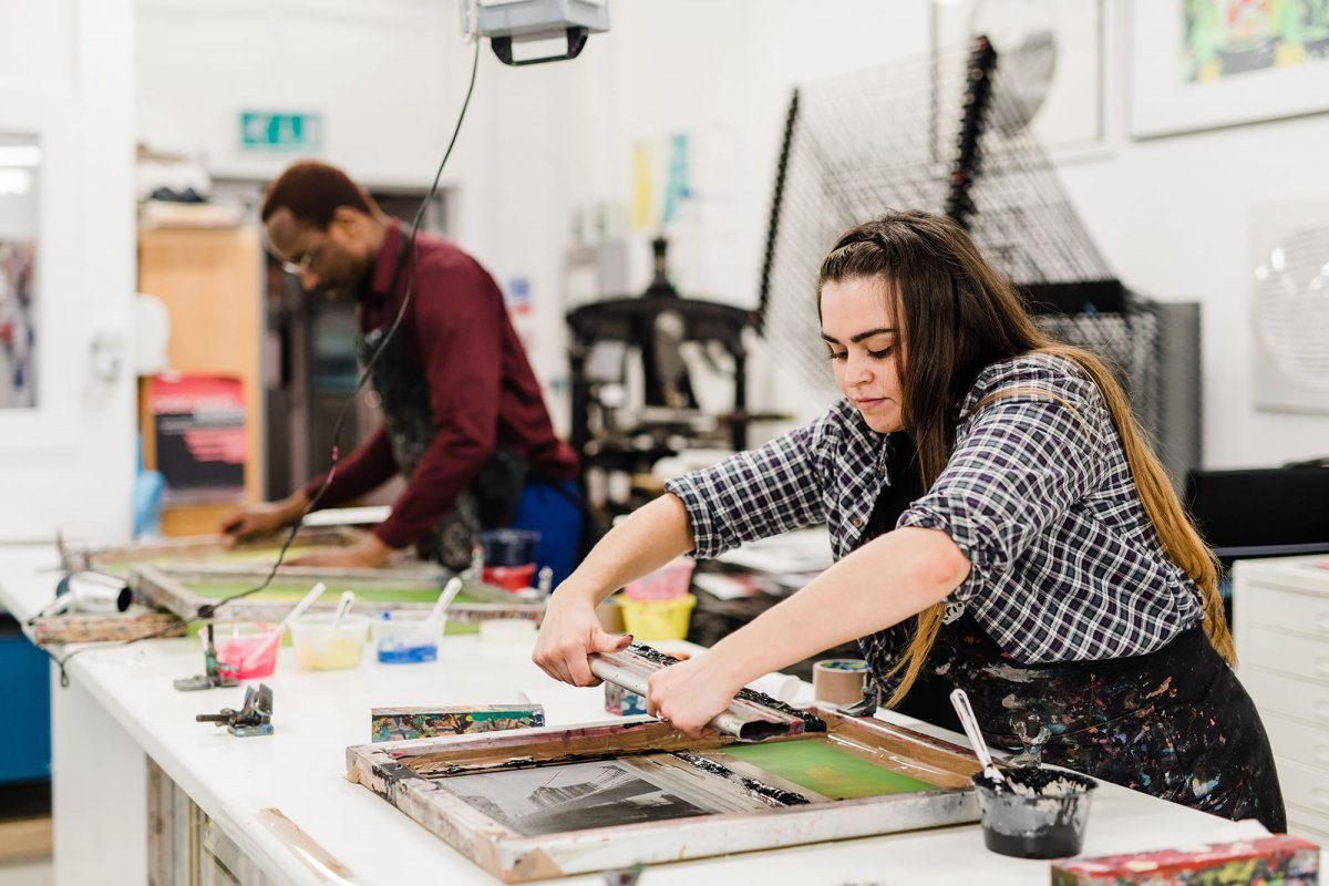 Two students working with screen printing equipment in the print room.