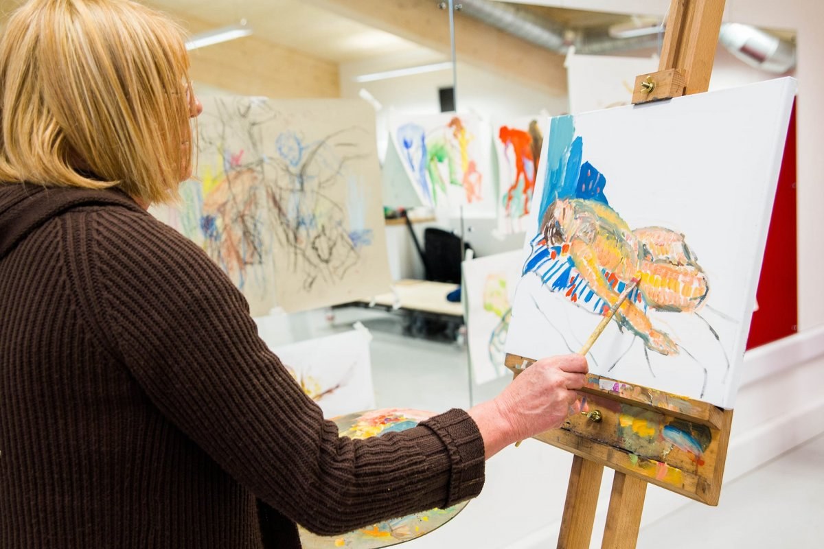 A student standing by an easel and painting on a canvas.