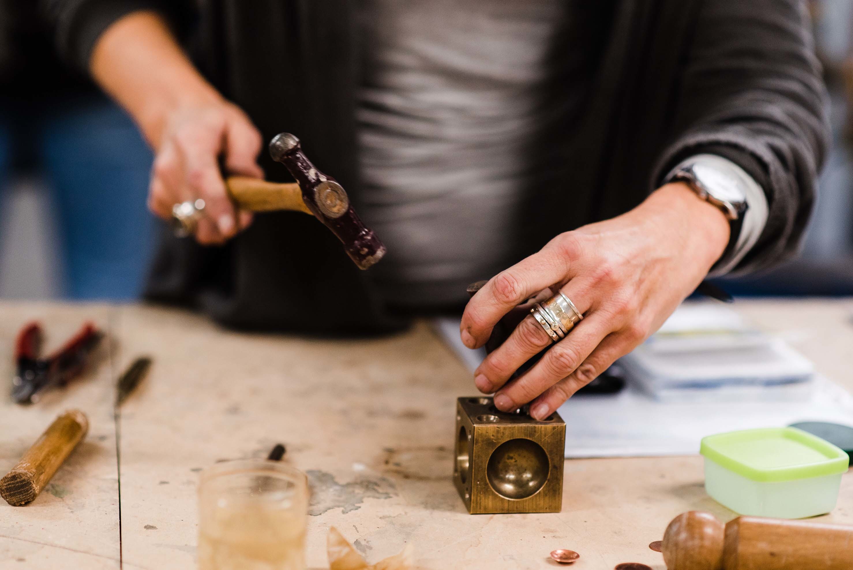 A person holds an object in place and raises a hammer to it.