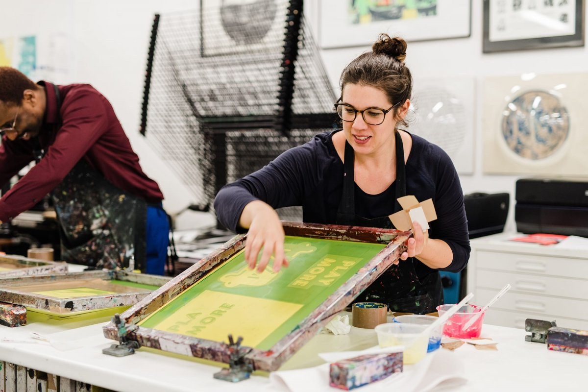 A student works in the print room with screen printing equipment.
