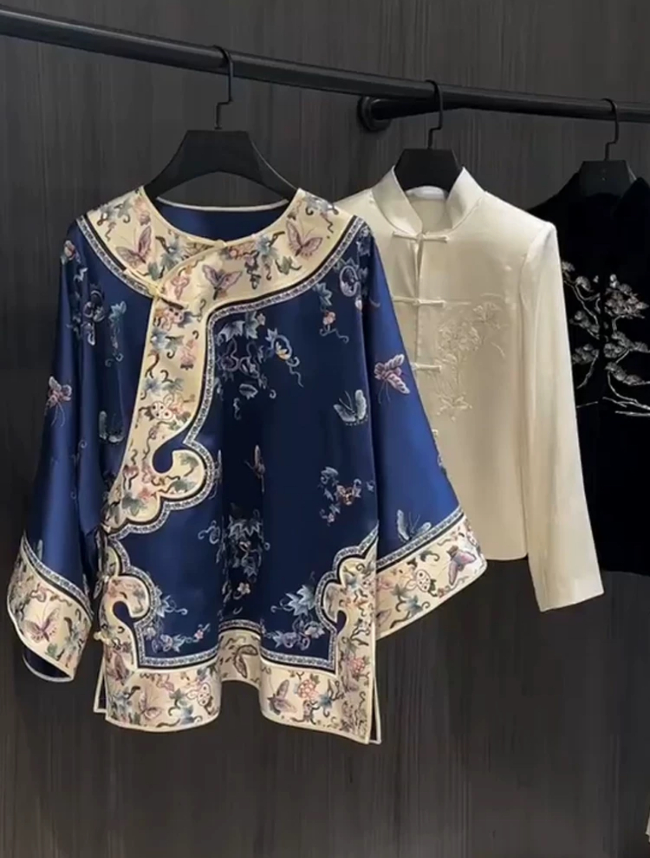 Three Chinese-style tops hanging on hangers on a clothes rail.