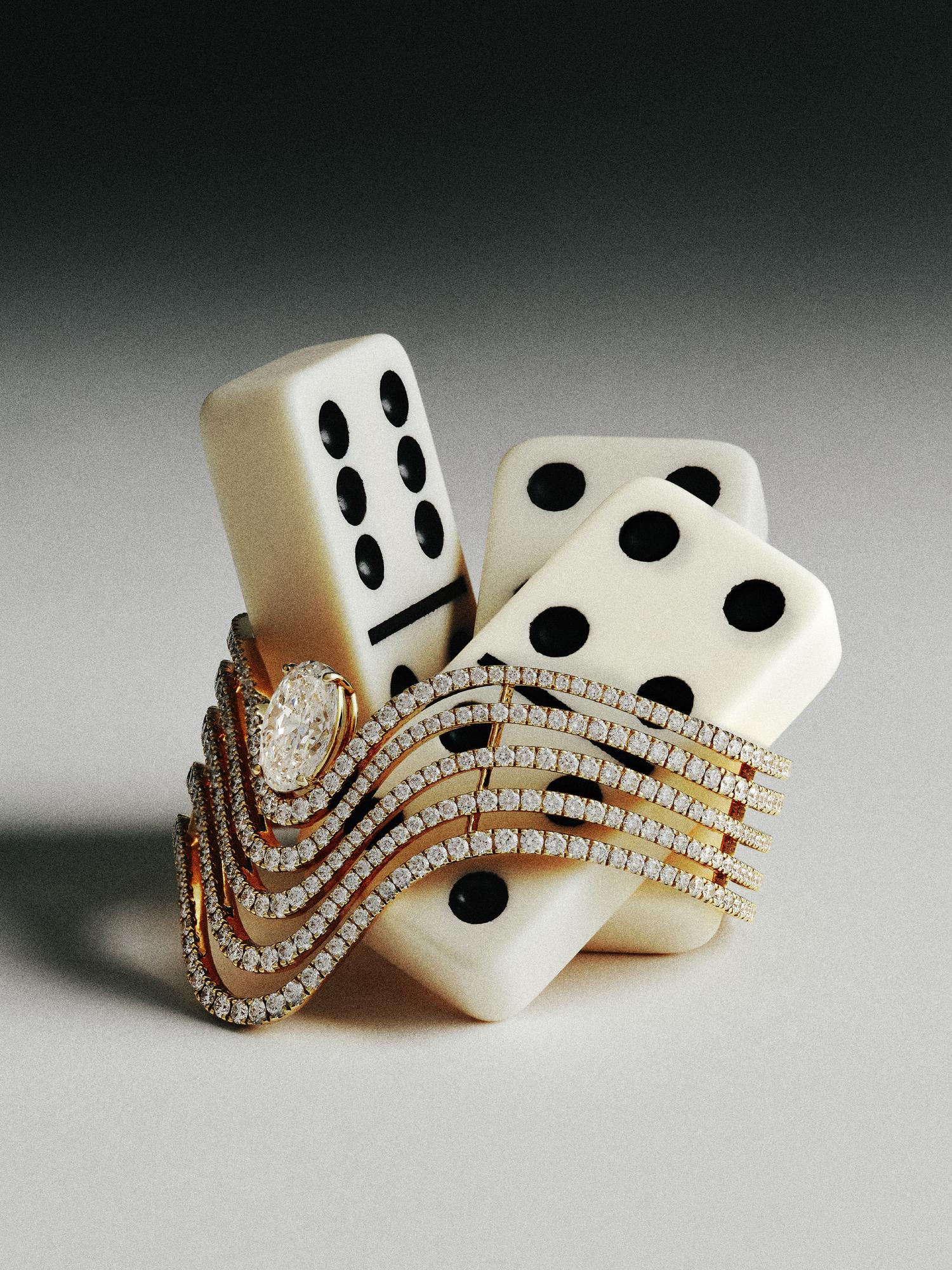 Three ivory dominoes with black dots arranged beside a golden bracelet adorned with numerous small diamonds, creating an elegant display against a neutral background.
