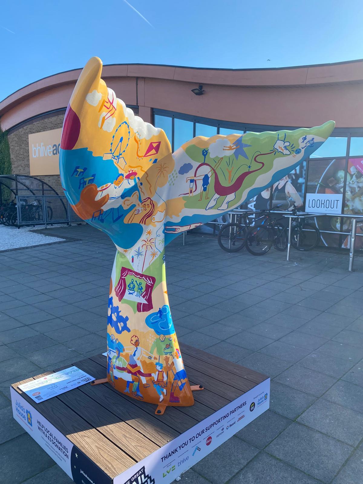 Sculpture of a giant mermaid tail with a colourful design, displayed on a pedestal outside BH Live, Bournemouth.