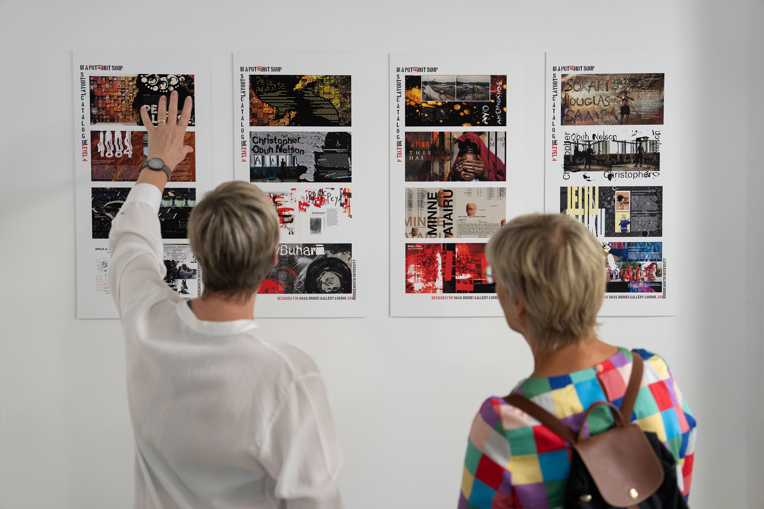 Two staff members standing and discussing BA (Hons) Graphic Design work from the Summer Shows 2022.