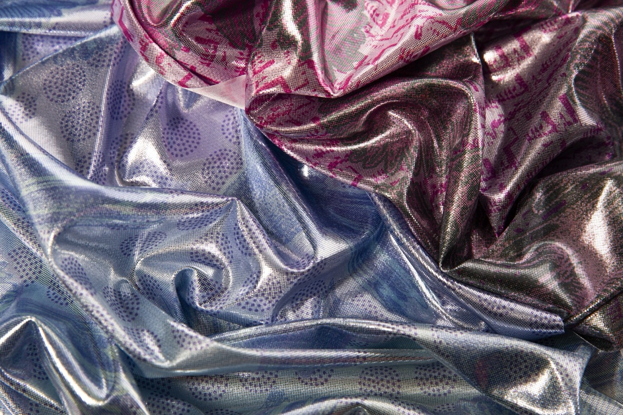Crumpled metallic fabrics in silver and burgundy with dotted patterns creating flowing, reflective folds and curves.
