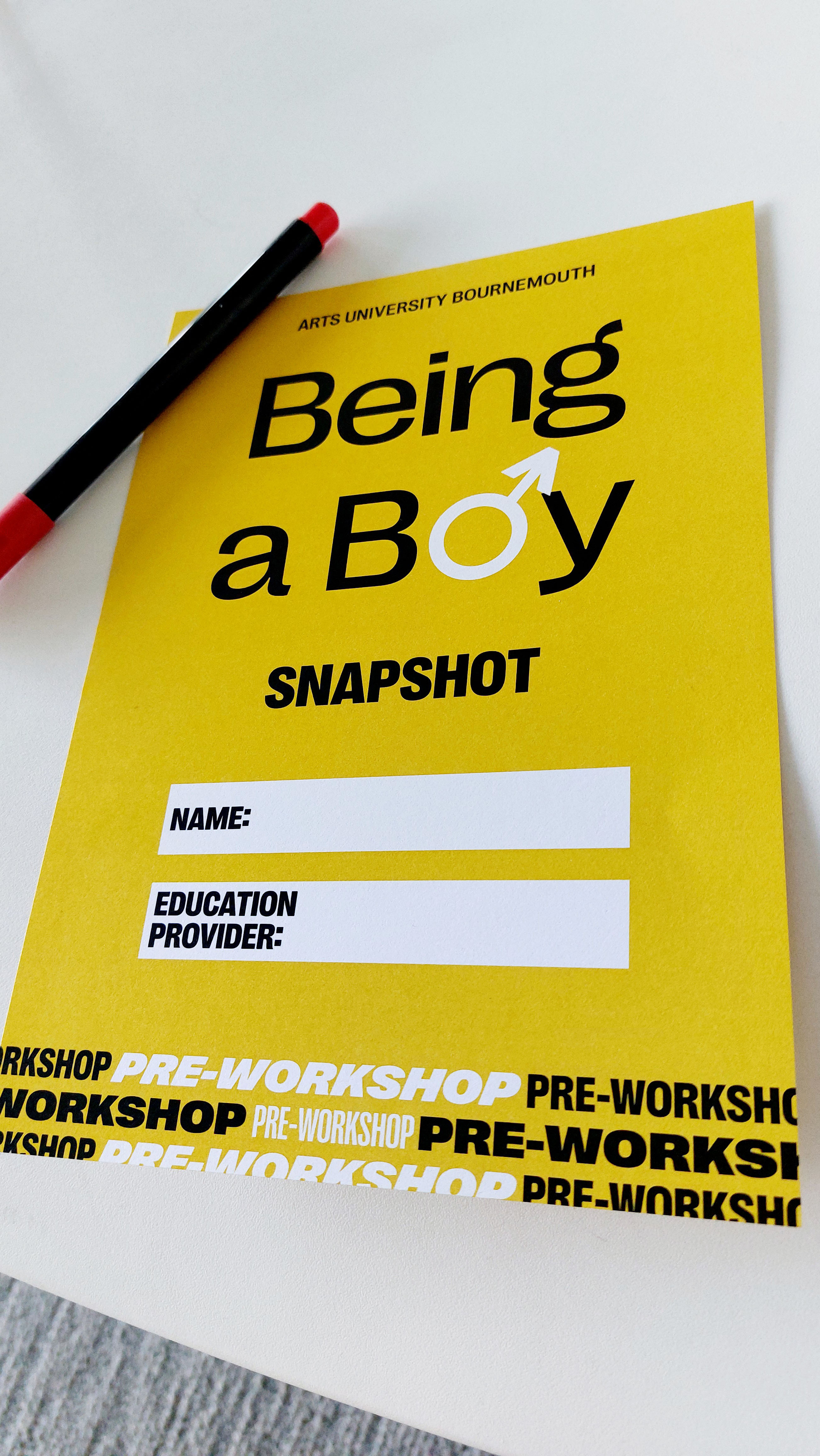 "Being a Boy SNAPSHOT" leaflet with white form fields and black pen with red cap on white surface.