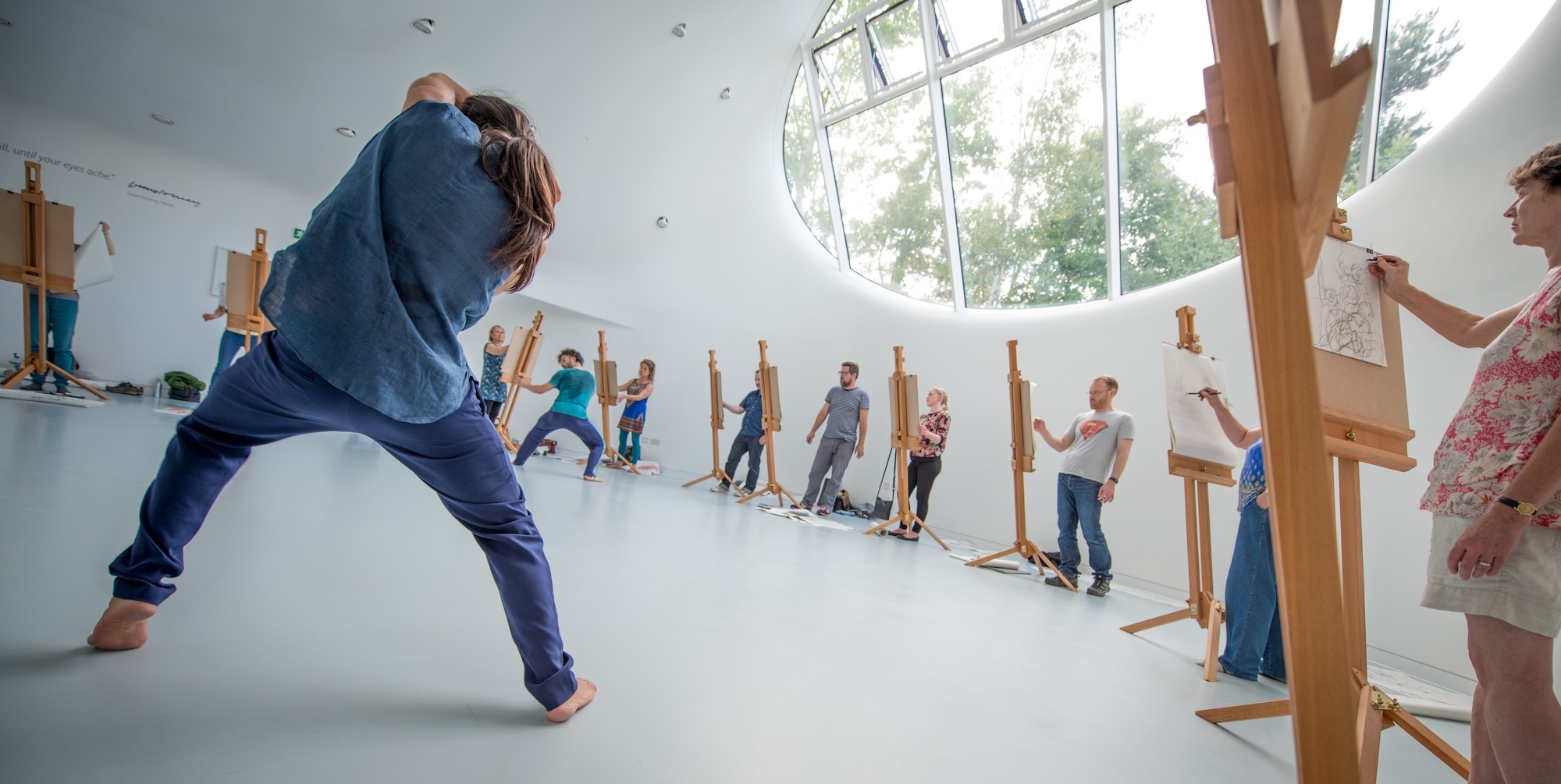Two performers pulling poses in the centre of a drawing studio while a circle of artists draw them.