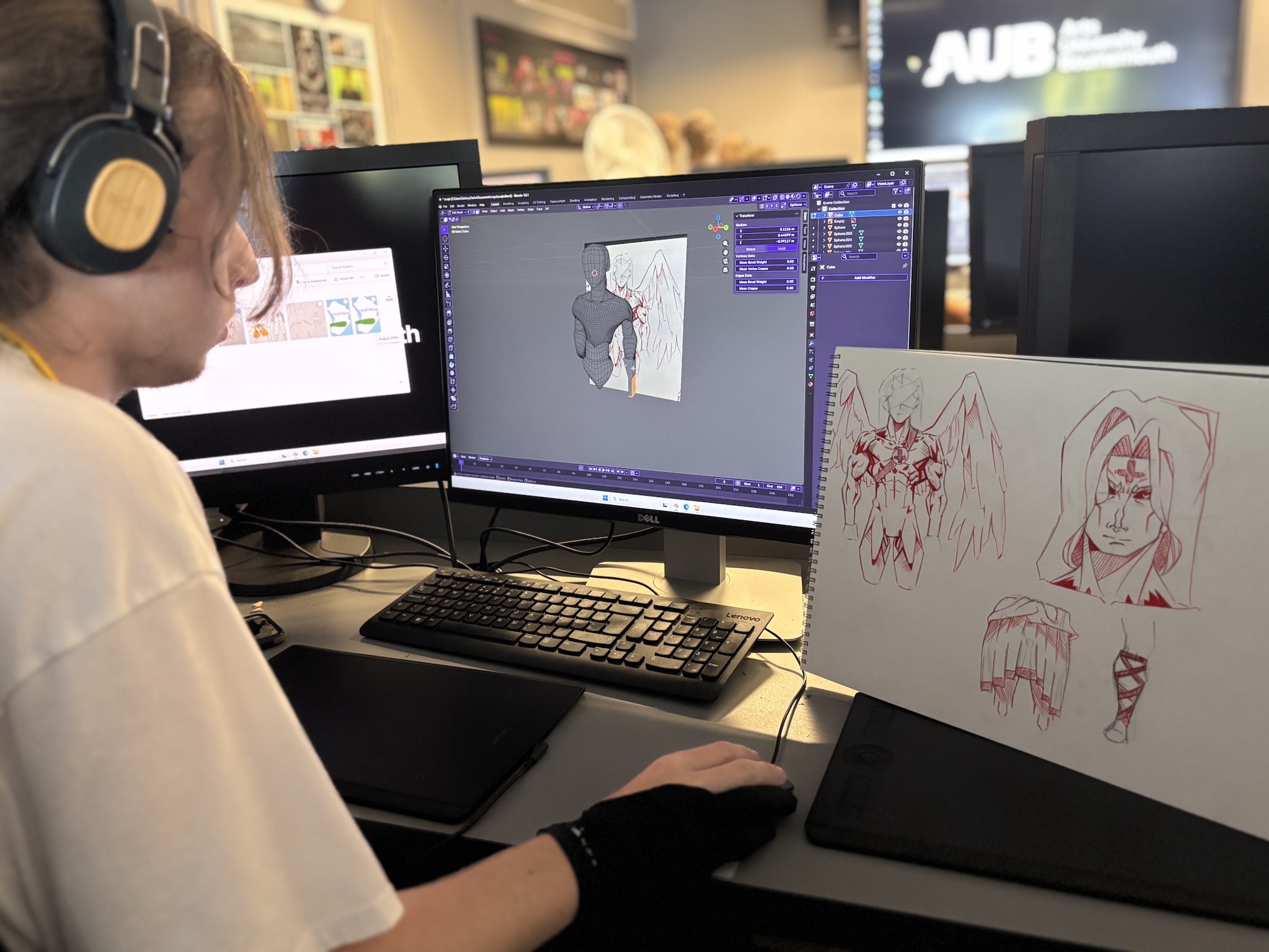 A person wearing headphones works at a desk with three monitors, drawing a character design in digital art software beside a sketchbook with red pencil sketches.