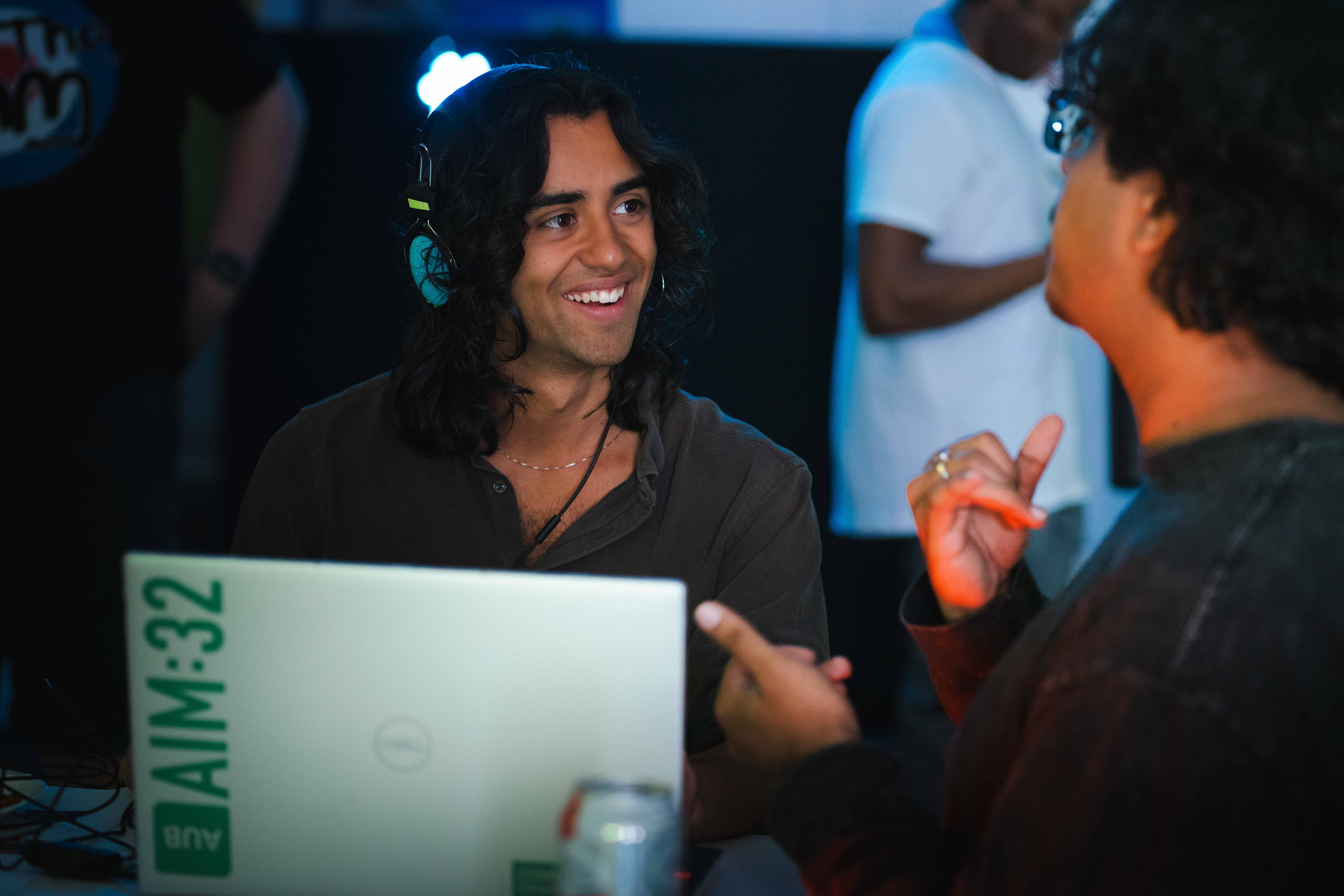 An Arts University Bournemouth student smiles while playing a video game on a laptop at a BA (Hons) Games Art and Design exhibition.