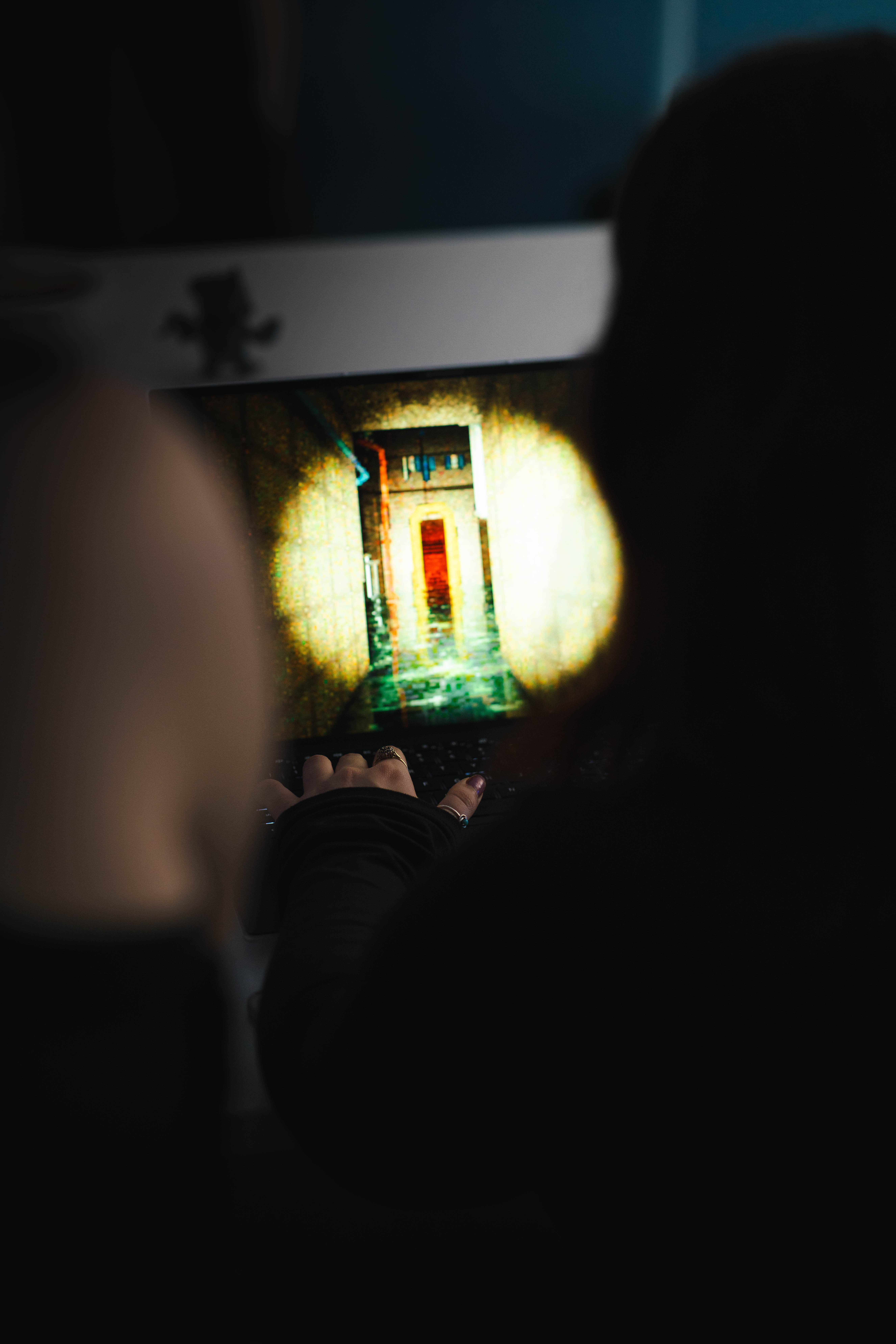 An Arts University Bournemouth student playing a video game on a laptop, viewed over the shoulder, at a BA (Hons) Games Art and Design exhibition event.