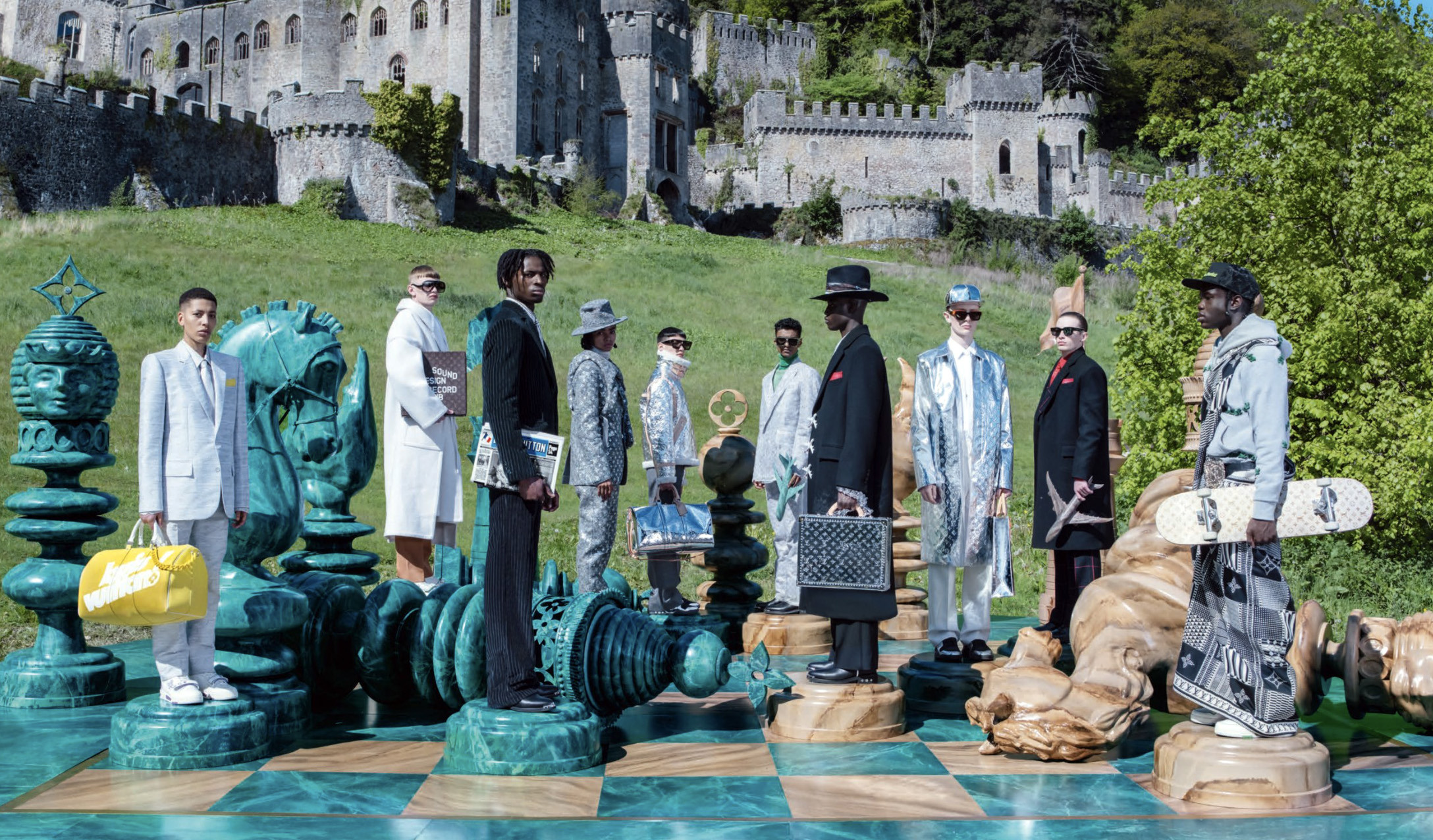 Several models in fashion costume stand as pieces on a giant chessboard in front of a castle