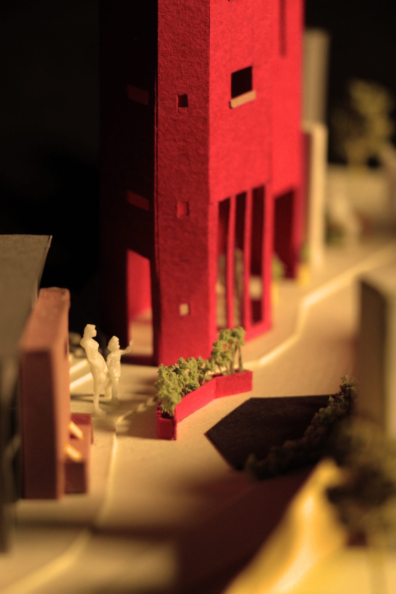 Architectural model with red rectangular tower, white curved platforms, and small green landscaping elements on cream base.