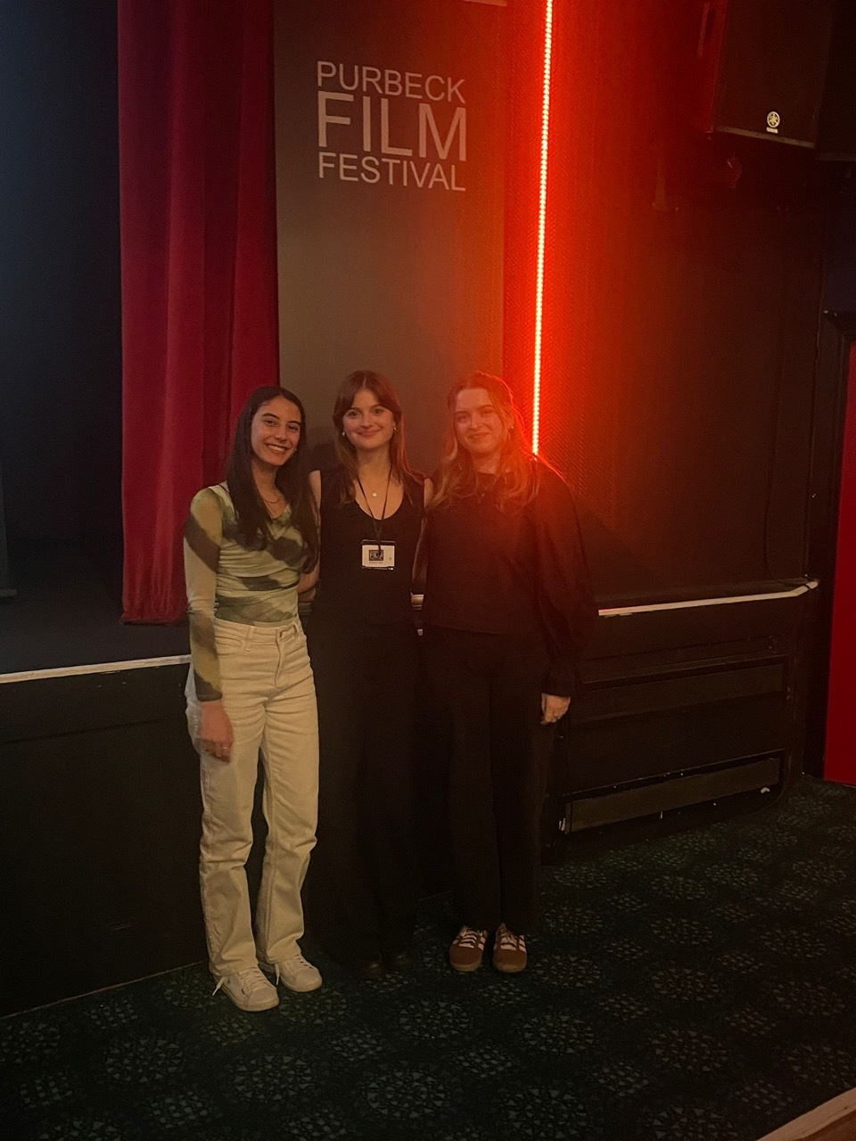 Three women stood inside at the Purbeck Film Festival with red lighting in the background.