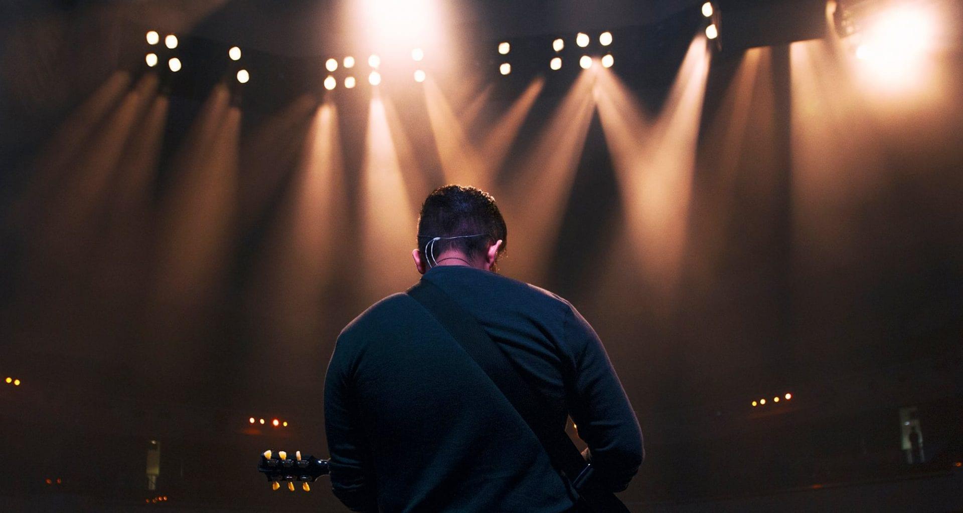 A man on stage, holding a guitar and facing away from the camera.