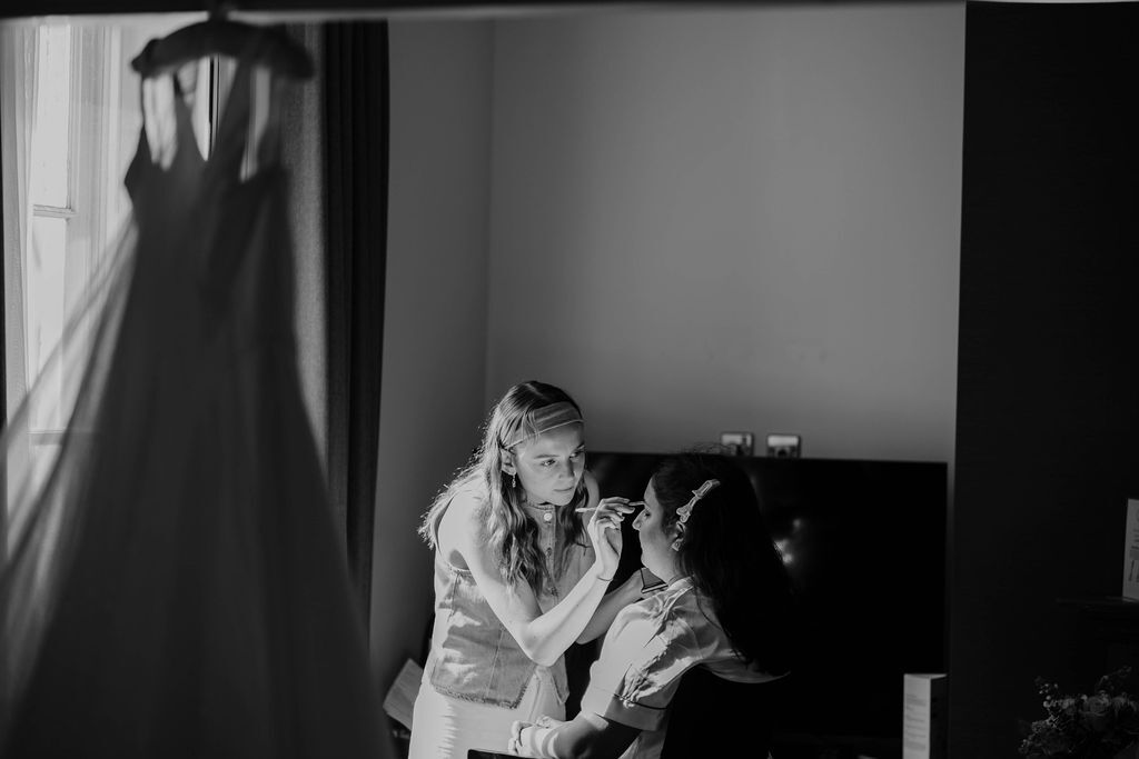 Black and white image of woman crouching beside large dog indoors, with dress hanging on door in background.
