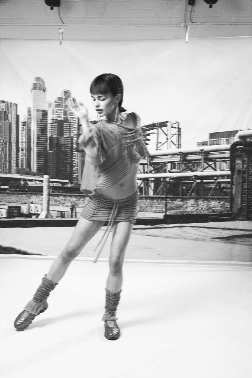 Black and white image of woman dancing with rooftop backdrop, city skyline with tall buildings and bridge.