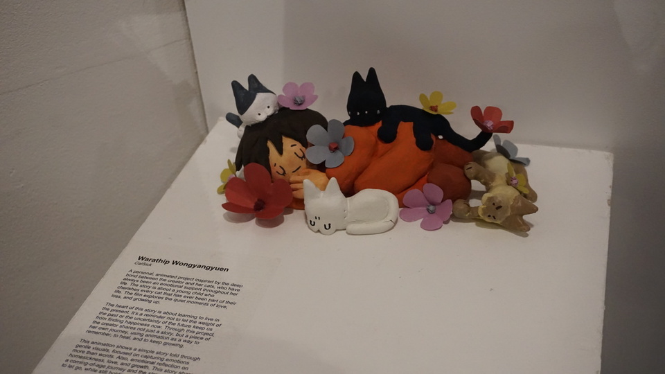 Museum display case with colourful fabric cat sculptures in various poses, accompanied by descriptive text panel below.