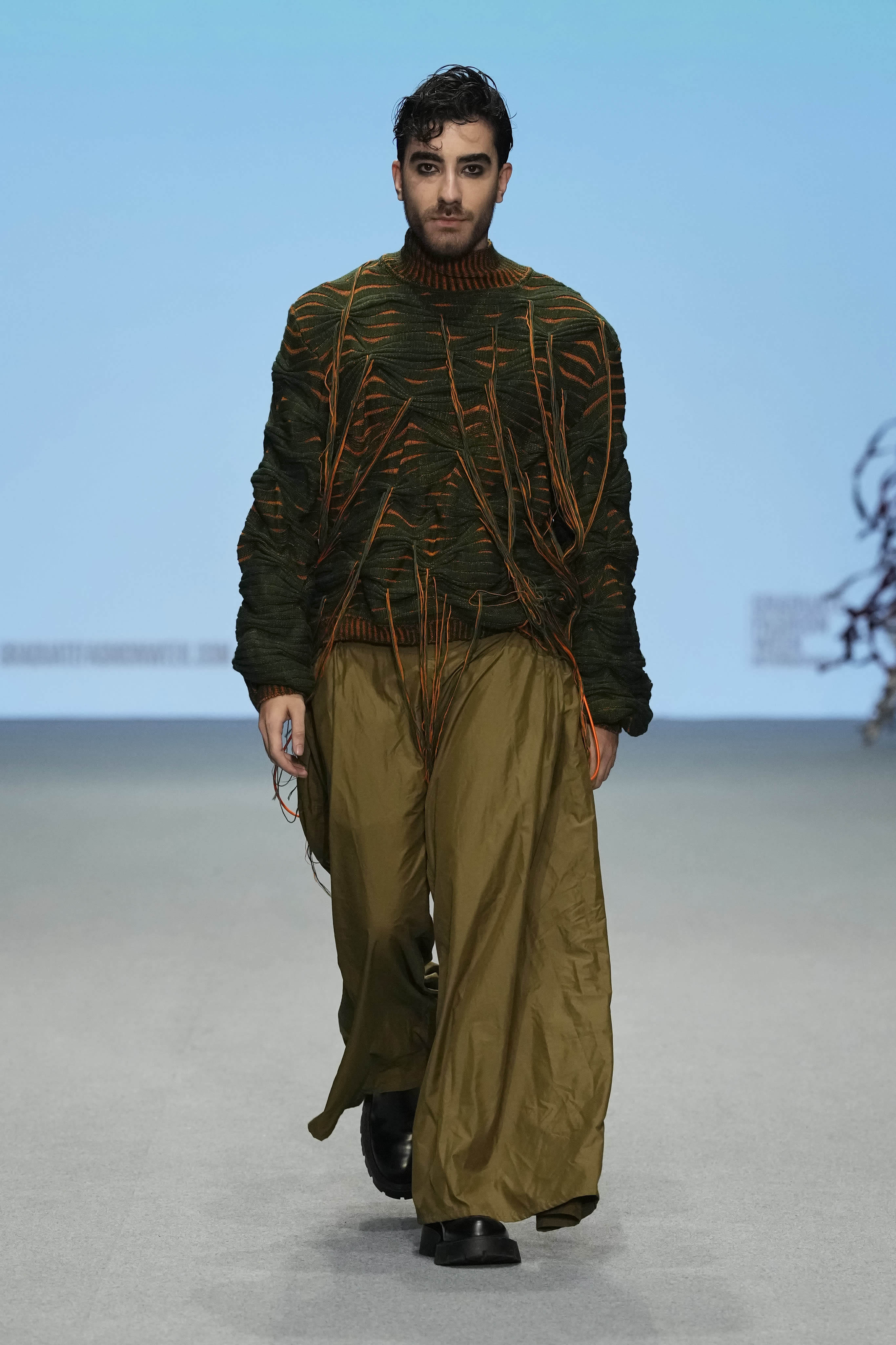 Male model walking down a runway at Graduate Fashion Week International 2023 in Dubai. They are wearing garments featured in the 51//NORTH collection by Lucy James.