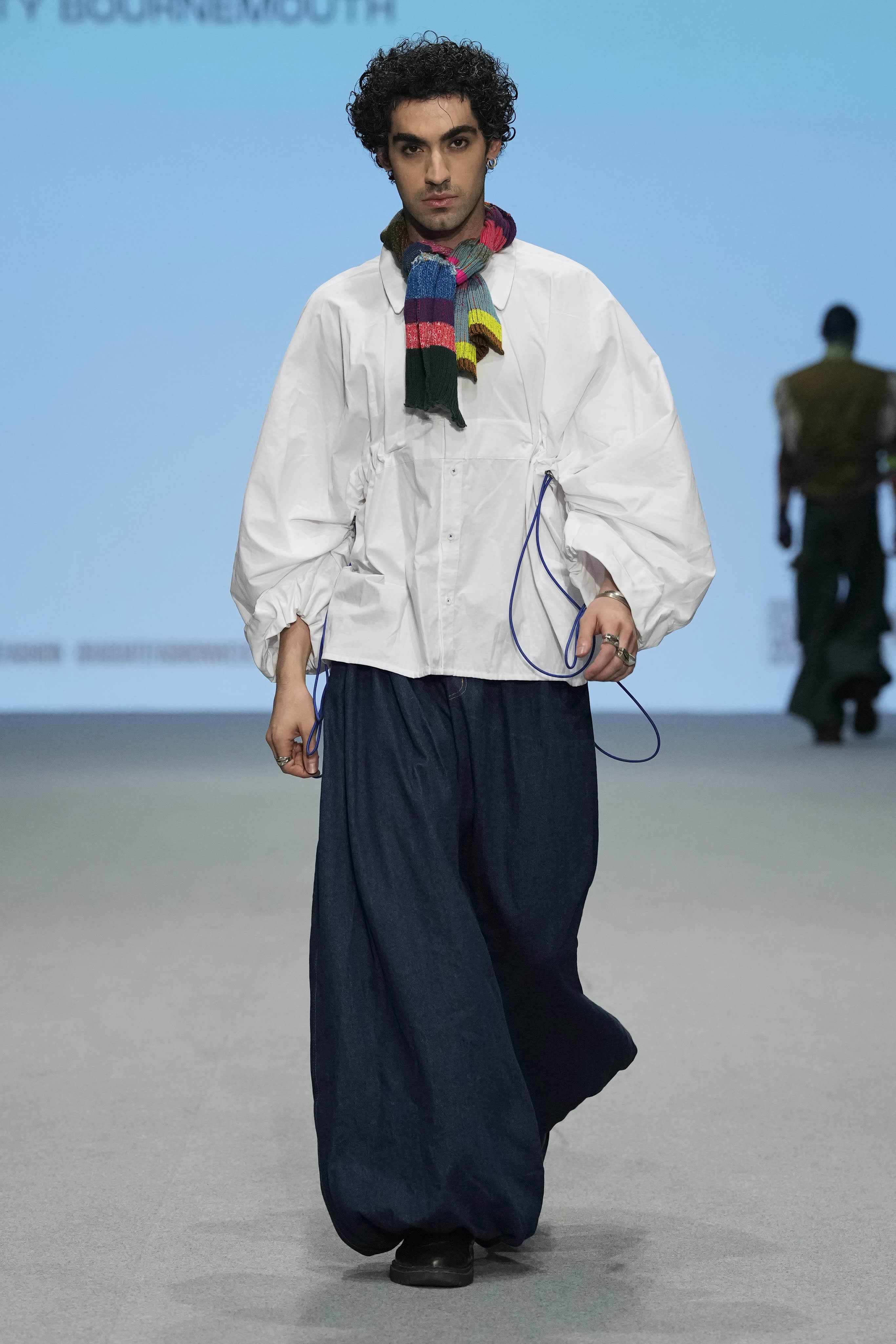 Male model walking down a runway at Graduate Fashion Week International 2023 in Dubai. They are wearing garments featured in the 51//NORTH collection by Lucy James.