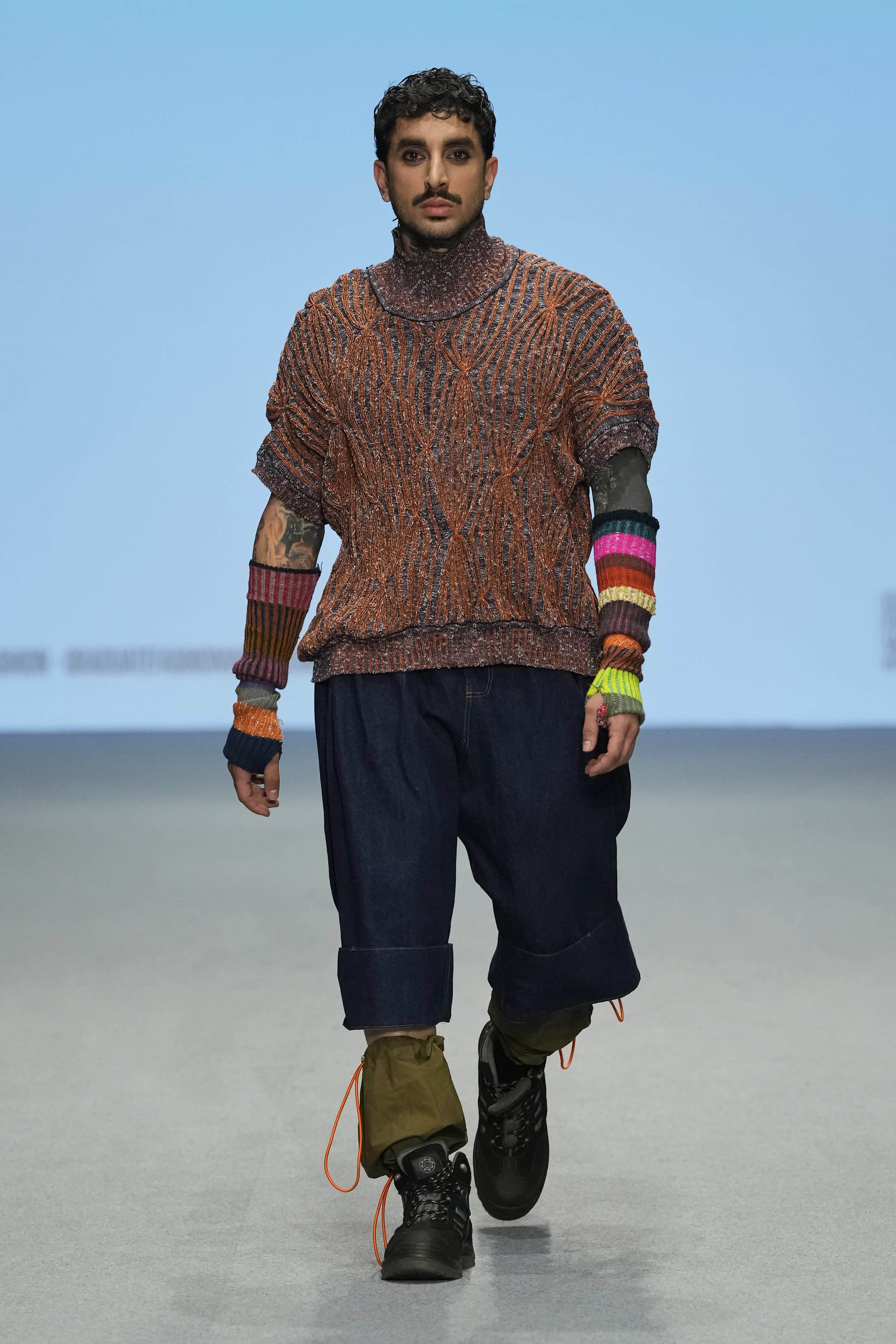 Male model walking down a runway at Graduate Fashion Week International 2023 in Dubai. They are wearing garments featured in the 51//NORTH collection by Lucy James.
