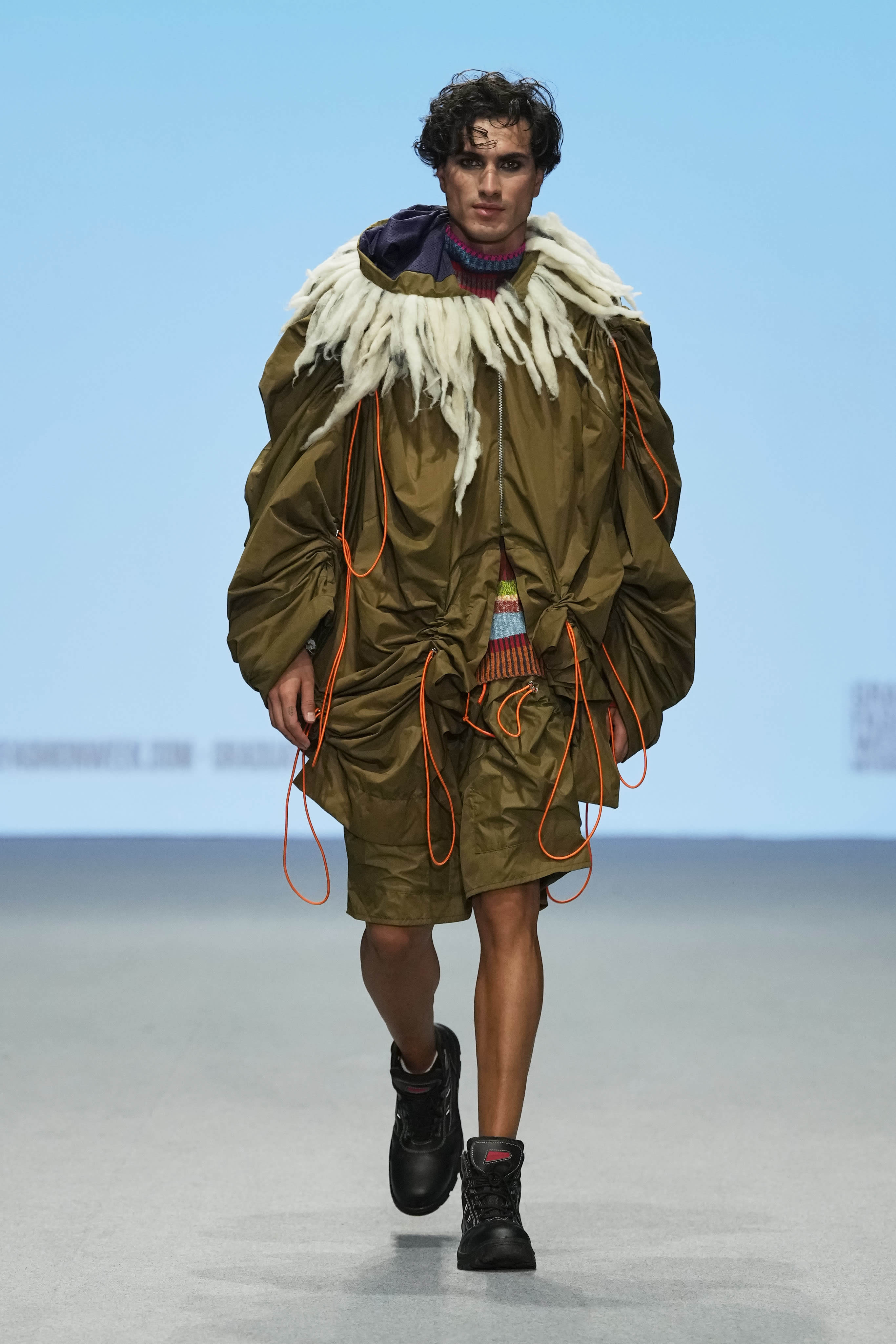 Male model walking down a runway at Graduate Fashion Week International 2023 in Dubai. They are wearing garments featured in the 51//NORTH collection by Lucy James.