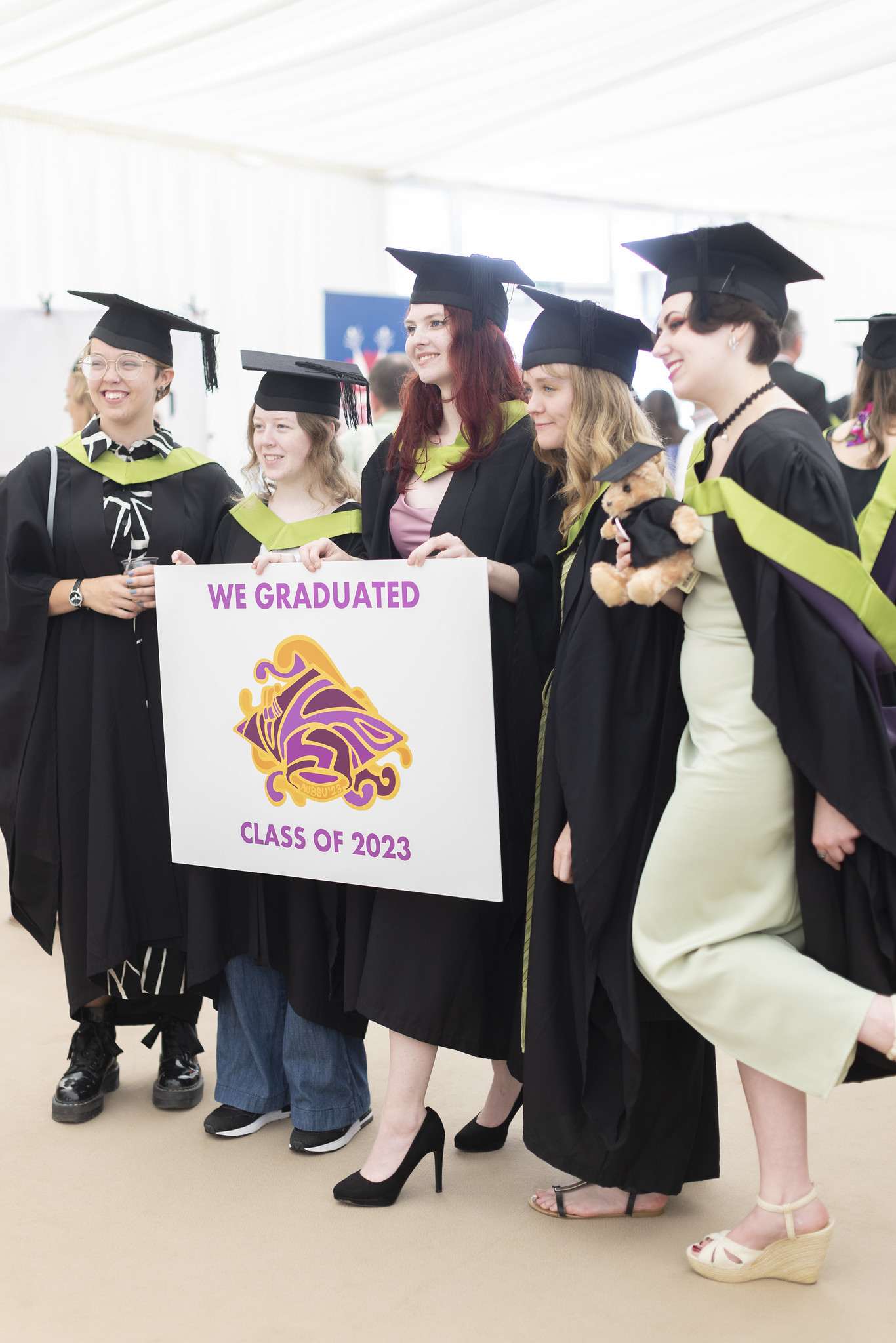 Five AUB graduates pose for a photo in the graduation marquee holding a sign reading "We graduated Class of 2023".