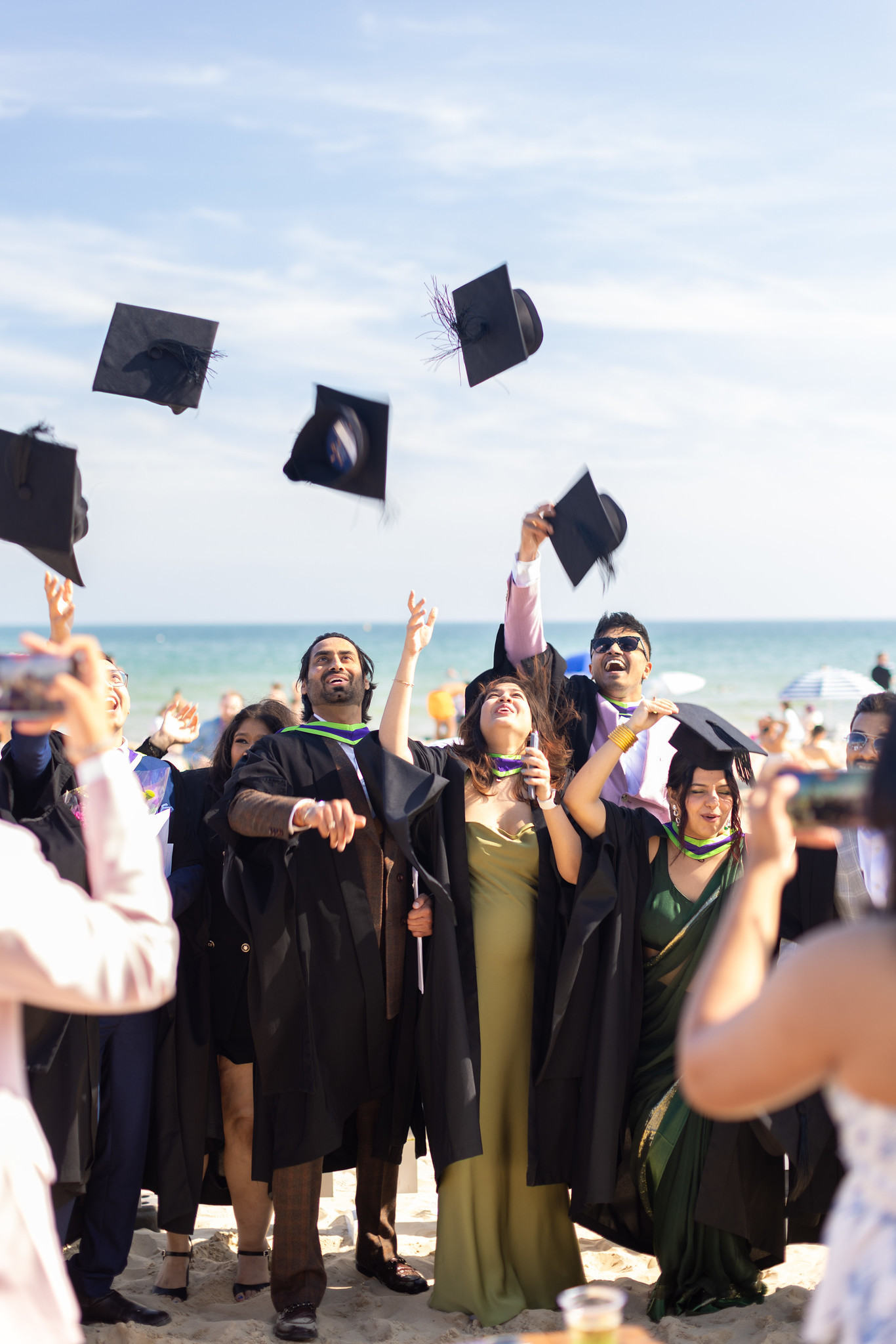 Graduates throwing their hats into the air on Bournemouth beach, blue sky.