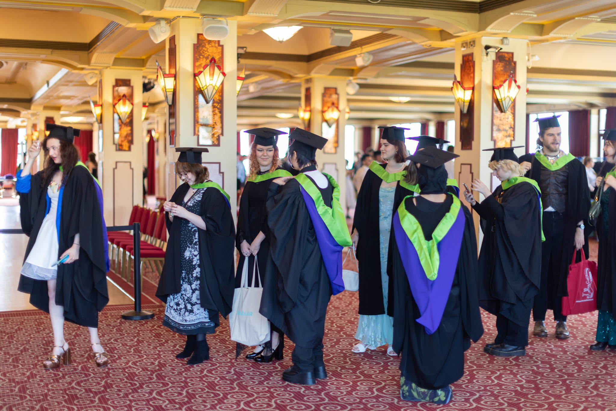 Students preparing for graduation in the Pavilion ballroom, black, green and purple robes.