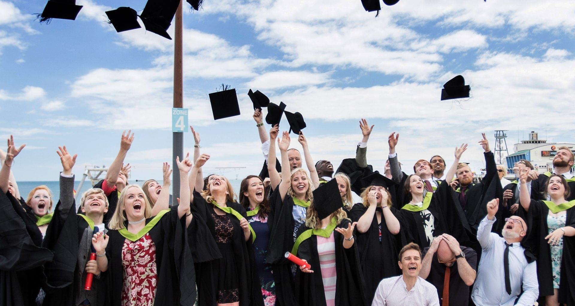 A large crowd of people in graduation dress throw their mortar boards into the air.