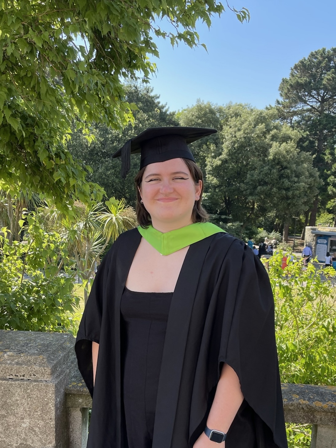 Nat Hawrylak graduating in a black and green gown in Bournemouth gardens.
