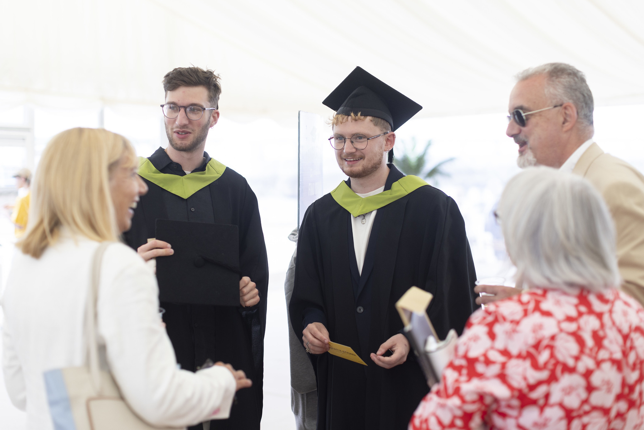 Two students talking to family members at graduation wearing gowns.